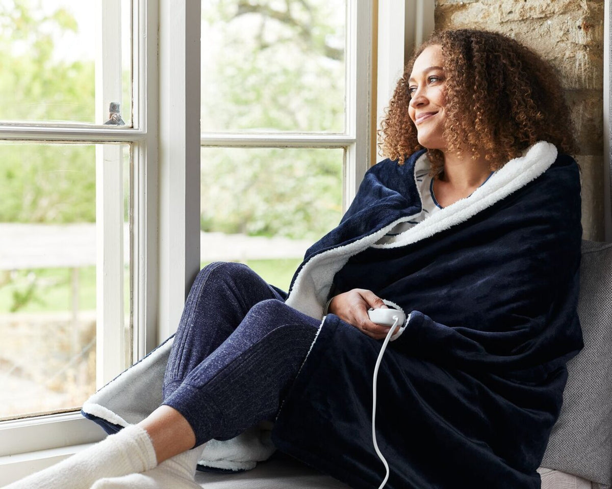 Person wrapped in an electric throw sitting at window