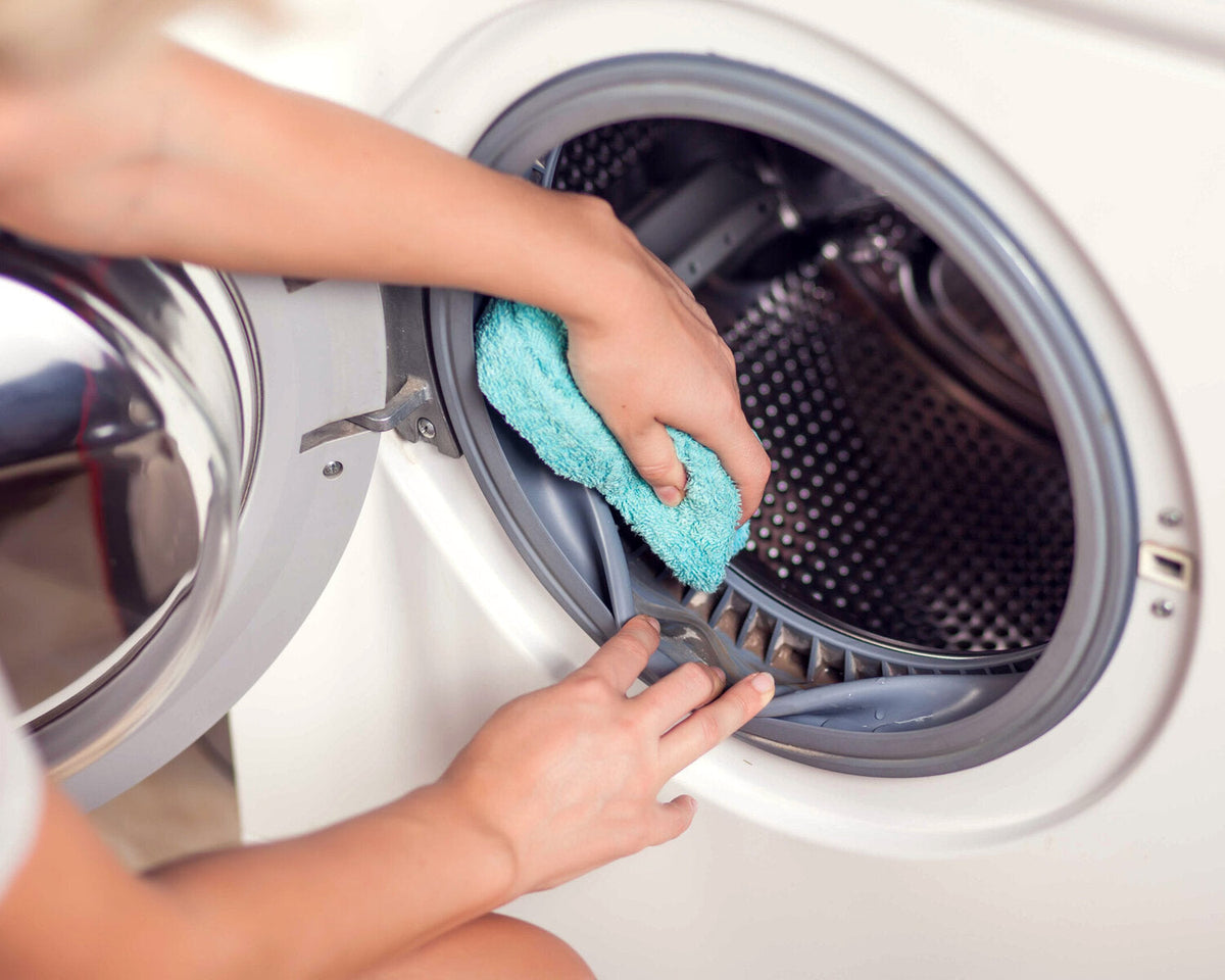 Person cleaning the rubber seal of a front-loading washing machine with a turquoise cloth.