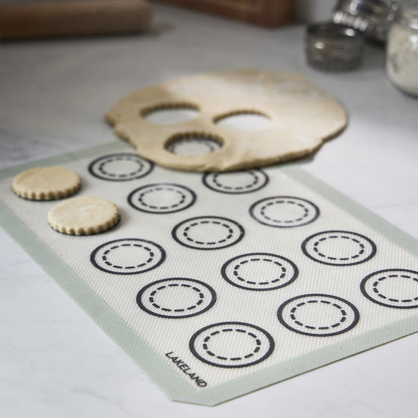 Biscuit dough is being cut out and placed on a silicone baking mat.
