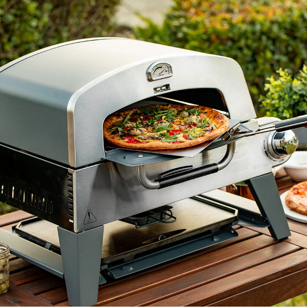 A pizza being taken out of the 3-in-1 Cuisinart BBQ, Grill and pizza oven.