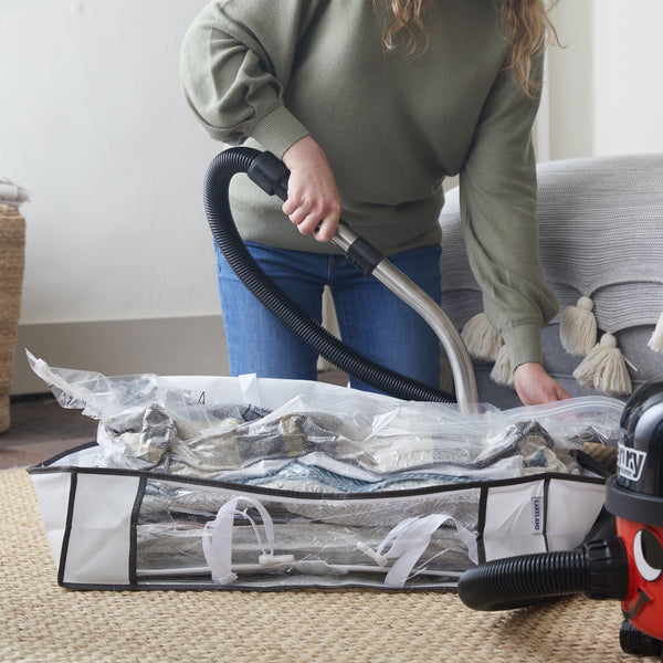 A lady is using a vacuum to take out the air of a Lakeland vacuum tote, which is full of clothes.