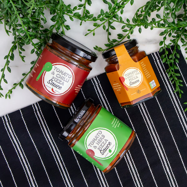 Three jars of Lakeland pizza sauces on a striped tea towel.