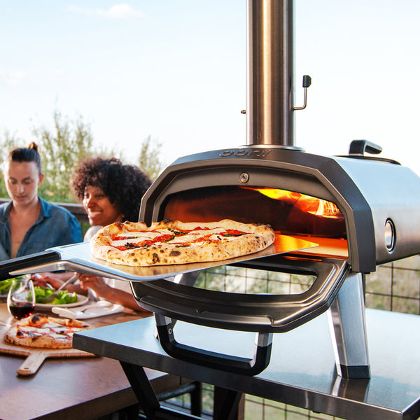 A freshly baked pizza being taken out of an Ooni pizza oven.