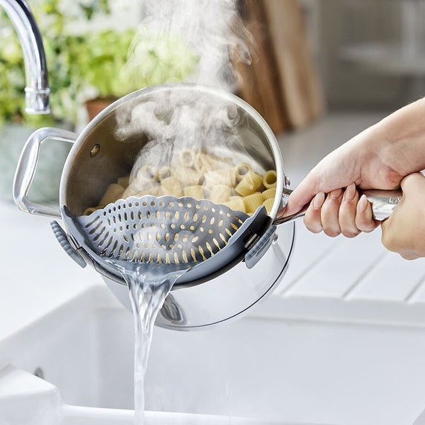 A clip-on pot strainer is being used to drain pasta above a sink.