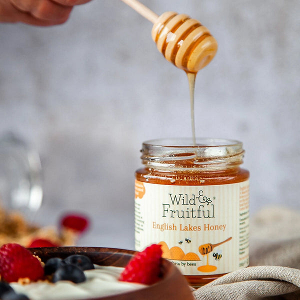 A honey dipper is being used to take honey out of a ar of natural honey.