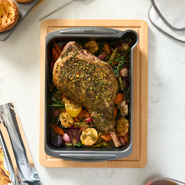 A top-down view of a roasting tray with a leg of lamb inside it.